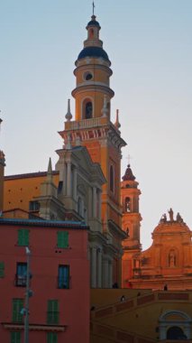 Menton, Fransa - 18 Mart 2025: St. Michel Bazilikası 'nın renkli binalarla çevrili uzak manzarası. Dikey