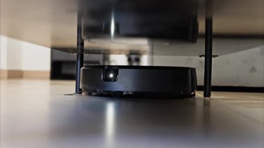 Evin yüzeyinin altını temizleyen küçük, siyah bir robot vakumunu kapat.