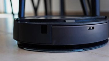 Küçük, siyah bir robot evi temizliyor.