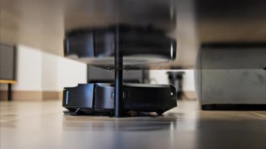 Evin yüzeyinin altını temizleyen küçük, siyah bir robot vakumunu kapat.
