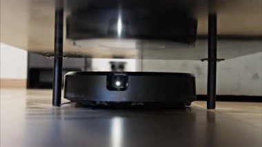 Evin yüzeyinin altını temizleyen küçük, siyah bir robot vakumunu kapat.