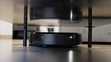 Evin yüzeyinin altını temizleyen küçük, siyah bir robot vakumunu kapat.
