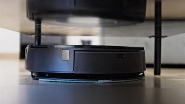 Evin yüzeyinin altını temizleyen küçük, siyah bir robot vakumunu kapat.