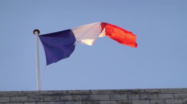 Fransa bayrağı mavi bir arka planda bir binanın tepesinde dalgalanıyor.