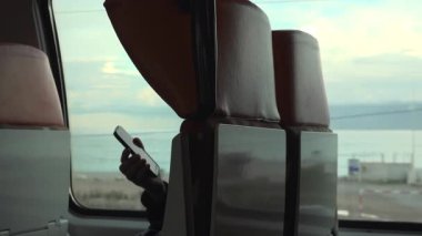 Hareket halindeki bir trenin cam koltuğunda telefonu tutan bir adam.