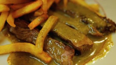 Tabağında et ve yeşil sos olan bir tabak patatesi yakın.