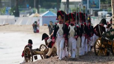 Golfe Juan, Fransa - 1 Mart 2025: Birden fazla adam yürüyüş yapıyor, kostüm giyiyor, Napolyon Bonaparte 'ın sahile inişini canlandırıyor