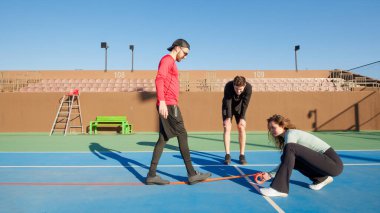 Bir grup yetişkin arkadaş bir tenis kortunu geçici kasetle Pickleball sahasına çeviriyor.