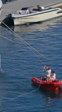 La Condamine, Monaco - 21 Ağustos 2024: 2 adam küçük, kırmızı şişme bir botta lüks bir yatın yanında. Dikey