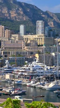 La Condamine, Monaco - 25 Ağustos 2024: Arka planda şehrin ufuk çizgisi olan Monako limanına yanaşmış birden fazla teknenin yakınında hareket eden bir tekne görüntüsü. Dikey