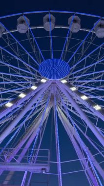 Akşamları arka planda mavi gökyüzü olan beyaz bir dönme dolabın görüntüsü. Dikey