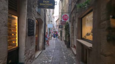 Saint Paul de Vence, Fransa - 19 Ağustos 2024: Şehrin dar, kaldırımlı bir caddesinde mağazaların yakınında yürüyen insanların görüntüsü