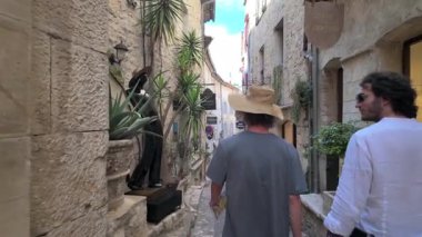 Saint Paul de Vence, Fransa - 19 Ağustos 2024: İnsanlar şehrin kaldırımlı sokaklarında bir heykelin yanında yürüyorlar