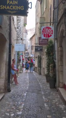 Saint Paul de Vence, Fransa - 19 Ağustos 2024: Şehrin dar, kaldırımlı bir caddesinde mağazaların yakınında yürüyen insanları görmek. Dikey