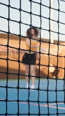 Kıvırcık saçlı bir kadının, bulanık bir arka planda mavi bir kortta pena topu oynadığı bir ağı kapat. Dikey