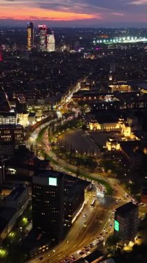 Akşamları İtalya, Milan 'da trafikte hareket eden arabaların insansız hava aracı görüntüsü. Dikey. Efsanevi kızıl gökyüzü ve mavi saat. Arkaplanda gökdelenler