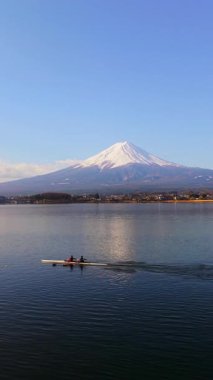 Fujikawaguchiko, Japonya - Arpil 23, 2025: Arkadaki Fuji Dağı ile birlikte Kawaguchiko Gölü 'nde kayık görüntüsü. Dikey