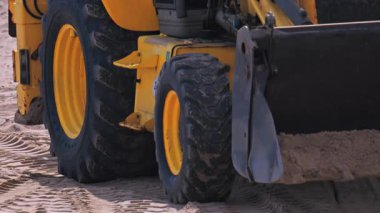 Kumlu sahilde hareket eden sarı yükleyicinin tekerleklerini kapatın.