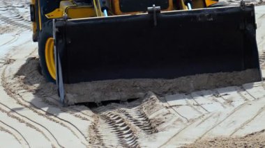 Kumsalda hareket eden sarı bir tekerlek yükleyicisinin yakınına.