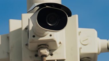 Arka planda mavi gökyüzü olan beyaz bir direğe monte edilmiş beyaz bir güvenlik kamerasını kapatın.