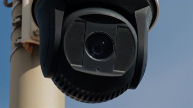 Yuvarlak, siyah güvenlik kamerası beyaz bir direğe monte edilmiş ve arka planda gökyüzü var.