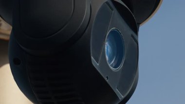 Yuvarlak, siyah güvenlik kamerası beyaz bir direğe monte edilmiş ve arka planda gökyüzü var.