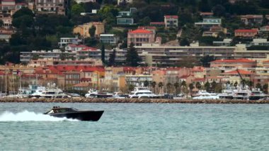 Juan-les-Pins, Fransa 'da liman ve arka planda binalar olan bir tekne denizde hareket ediyor.