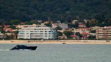 Juan-les-Pins, Fransa 'da sahilde ve arka planda binaları olan bir tekne denizde hareket ediyor.