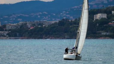 Yelkenli yelkenli şehir ve dağ ile birlikte denizde ilerliyor.