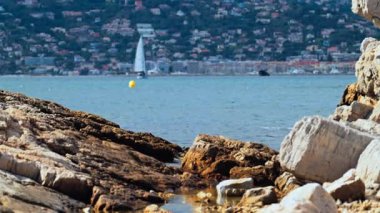 Kıyıdaki kayalıklar Juan-les-Pins 'de denizde ilerleyen bir yelkenli yelkenli, Fransa' da şehir ve arka planda dağ.