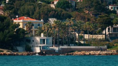 Distant view of multiple villas on the shore with the waves of the sea crashing on the rocks