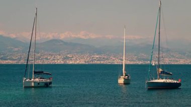 Arka planda Fransız Rivierası 'nın binaları ve dağlarıyla denizde yüzen tekneler.