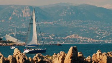 Yelkenli yelkenli şehir ve dağ ile birlikte denizde ilerliyor.