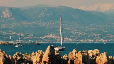 Yelkenli yelkenli şehir ve dağ ile birlikte denizde ilerliyor.