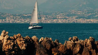 Yelkenli yelkenli şehir ve dağ ile birlikte denizde ilerliyor.