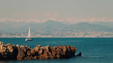 Yelkenli yelkenli şehir ve dağ ile birlikte denizde ilerliyor.