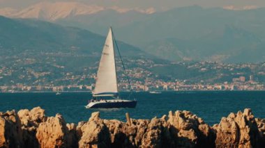 Yelkenli yelkenli şehir ve dağ ile birlikte denizde ilerliyor.