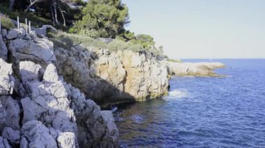 Antibes, Fransa - 5 Nisan 2025 Akdeniz 'in dalgaları Fransız Rivierası kıyısındaki kayalara çarpıyor ve insanlar oluşumlar üzerinde yürüyor.