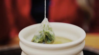 Kırmızı elbiseli bir kadının yeşil çay poşetini beyaz bir fincana bandırdığı yakın plan.