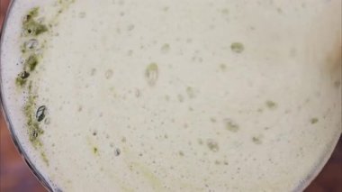 Close up of a woman mixing the foam on a matcha latte with a paper straw on a wooden tray