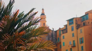 Menton, France Distant view of the St Michel Basilica surrounded by colourful buildings and palm trees