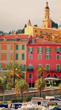 Menton, France Distant view of the St Michel Basilica surrounded by colourful buildings and palm trees. Vertical