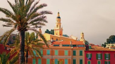 Menton, Fransa 'nın St. Michel Bazilikası manzarası renkli binalar ve palmiye ağaçları ile çevrili.