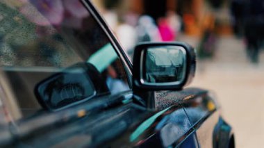 Yağmurda siyah bir arabanın aynasını kapat. İnsanlar arka planda bulanık bir şekilde yürüyor.