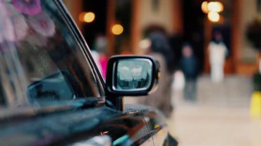 Yağmurda siyah bir arabanın aynasını kapat. İnsanlar arka planda bulanık bir şekilde yürüyor.