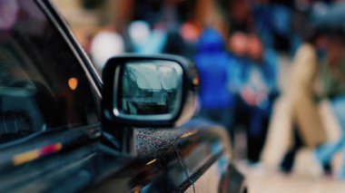 Yağmurda siyah bir arabanın aynasını kapat. İnsanlar arka planda bulanık bir şekilde yürüyor.