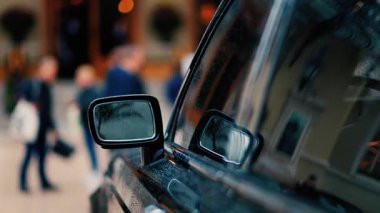 Yağmurda siyah bir arabanın aynasını kapat. İnsanlar arka planda bulanık bir şekilde yürüyor.