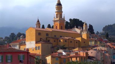 Menton, Fransa St Michel Bazilikası 'nın uzak manzarası bulutlu bir günde renkli binalar ve palmiye ağaçları ile çevrilidir.