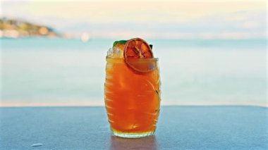 Arka planda bulanık deniz manzaralı bir masanın üzerindeki portakal kokteylini kapat.