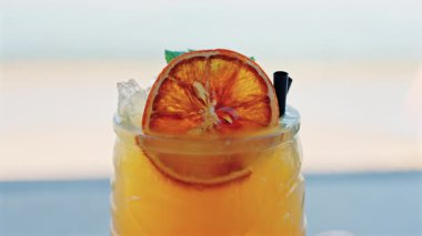Arka planda bulanık deniz manzaralı bir masanın üzerindeki portakal kokteylini kapat.